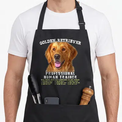 Professional golden retriever apron - Realistic golden retriever head with white title and light green list of nine — shown on a black cotton canvas apron against a white background