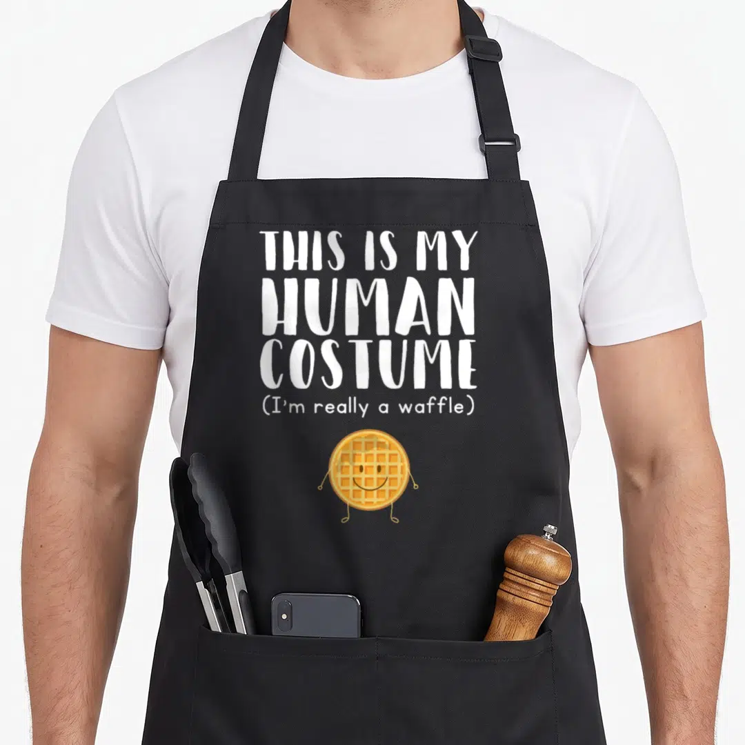 Human honestly apron - Cartoon waffle character below stacked white text reading human costume — shown on a black cotton canvas apron against a white background