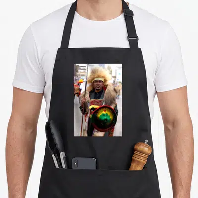 Oromo ethiopian boy apron - Man in traditional dress holding spear and shield with tan red green yellow colors — shown on a black cotton canvas apron against a white background