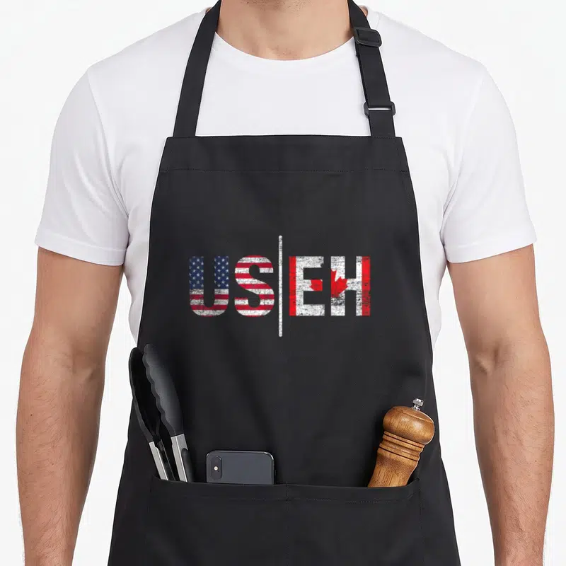 Pride useh american flag apron - US and EH text filled with red white blue flag patterns separated by a vertical line — shown on a black cotton canvas apron against a white background