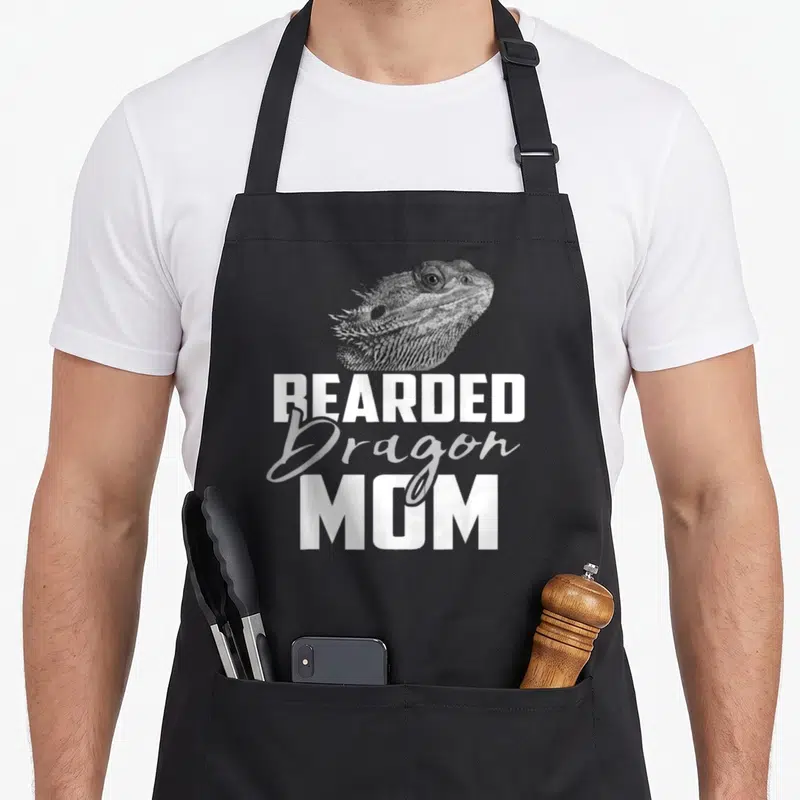 Funny lizard dragon apron - Bearded dragon head photo above stacked white and grey text reading Bearded Dragon Mom — shown on a black cotton canvas apron against a white background