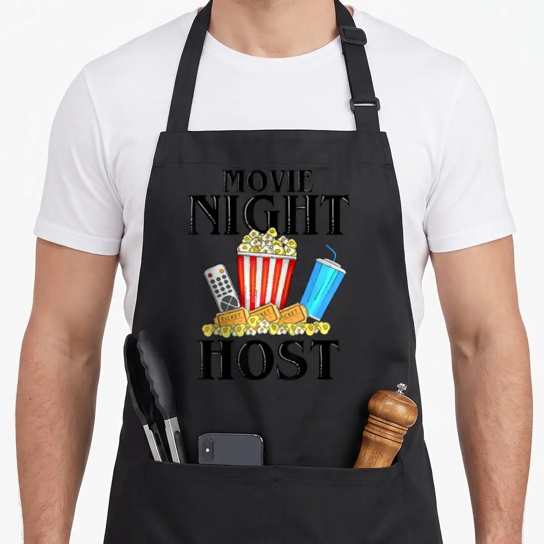 Host family aprons - Movie Night Host text surrounding a popcorn bucket, remote, blue drink, and tickets in cartoon — shown on a black cotton canvas apron against a white background