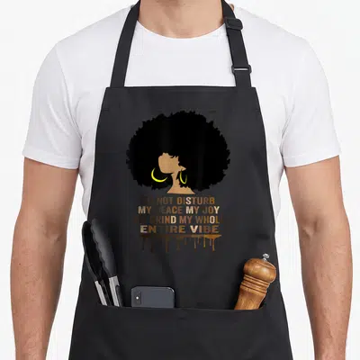 Joy entire grind apron - Woman afro silhouette with yellow hoops and stacked text Do Not Disturb My Peace My Joy My — shown on a black cotton canvas apron against a white background