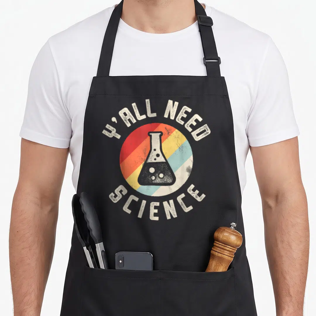Yall chemistry apron - Retro erlenmeyer flask on red orange yellow blue striped circle with Y ALL NEED SCIENCE text — shown on a black cotton canvas apron against a white background