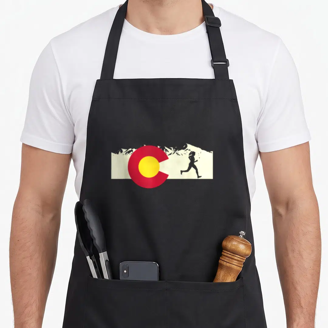 Run pride apron - Grey runner silhouette next to red circle yellow center white mountain peaks — shown on a black cotton canvas apron against a white background