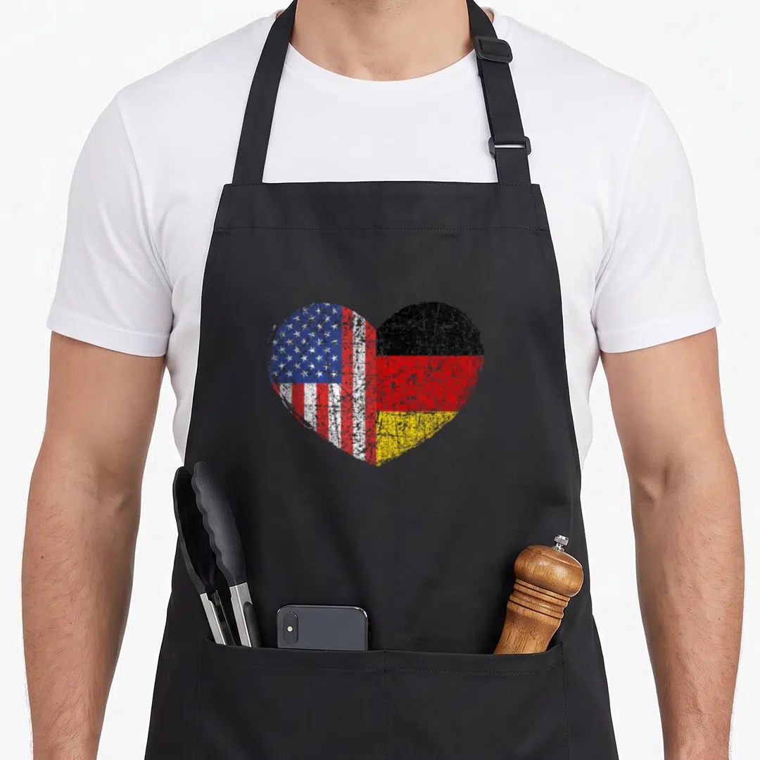 Dual germany apron - Heart split into US and German flag sections with distressed red white blue black gold — shown on a black cotton canvas apron against a white background