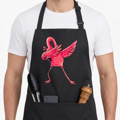 Dabbing flamingo apron - Cartoon pink flamingo in a dab pose with black outlines — shown on a black cotton canvas apron against a white background