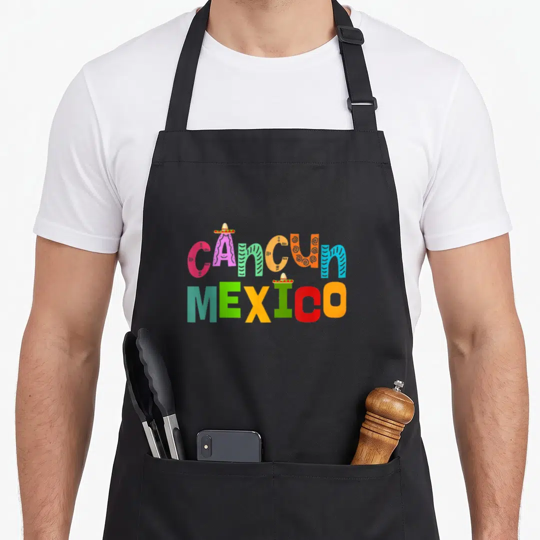 Typography mexico apron - Stacked colorful CANCUN MEXICO text with small sombrero icons on letters — shown on a black cotton canvas apron against a white background