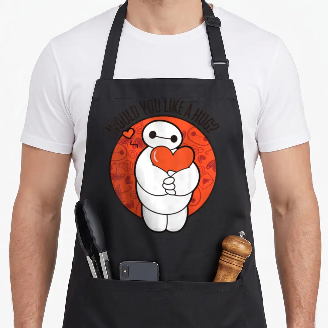 Hero valentine's day apron - Baymax character holding red heart inside circle with arched text WOULD YOU LIKE A HUG — shown on a black cotton canvas apron against a white background
