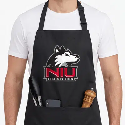 Northern husky apron - Cartoon husky head above red NIU text and white HUSKIES bar — shown on a black cotton canvas apron against a white background