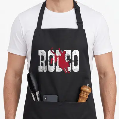 Rider western aprons - RODEO text with red bull rider silhouette, distressed white and red print — shown on a black cotton canvas apron against a white background