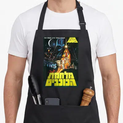 Hope hebrew aprons - Star Wars poster with Luke Skywalker, Vader helmet, robots, and yellow Hebrew text — shown on a black cotton canvas apron against a white background