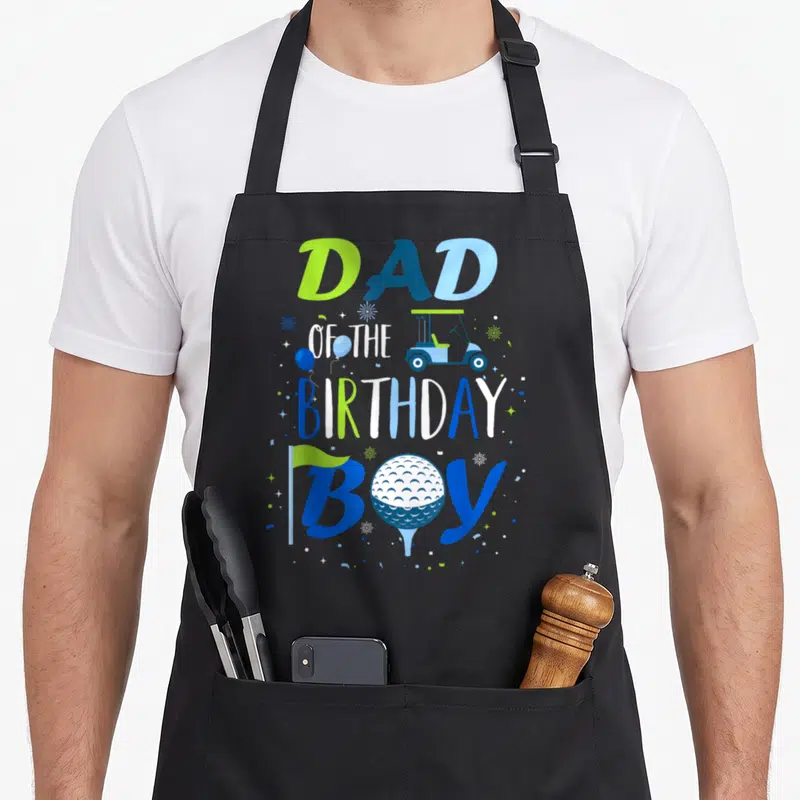 Birthday golf apron - DAD OF THE BIRTHDAY BOY text with golf cart, ball, flag, and confetti in blue and green — shown on a black cotton canvas apron against a white background