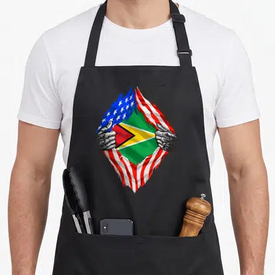 Guyana american flag apron - Two hands rip USA flag to show Guyanese flag below, red white blue green yellow — shown on a black cotton canvas apron against a white background