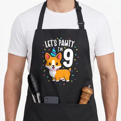 9th corgi apron - Cartoon corgi with party hat and text LET'S PAWTY I'M 9 with confetti — shown on a black cotton canvas apron against a white background