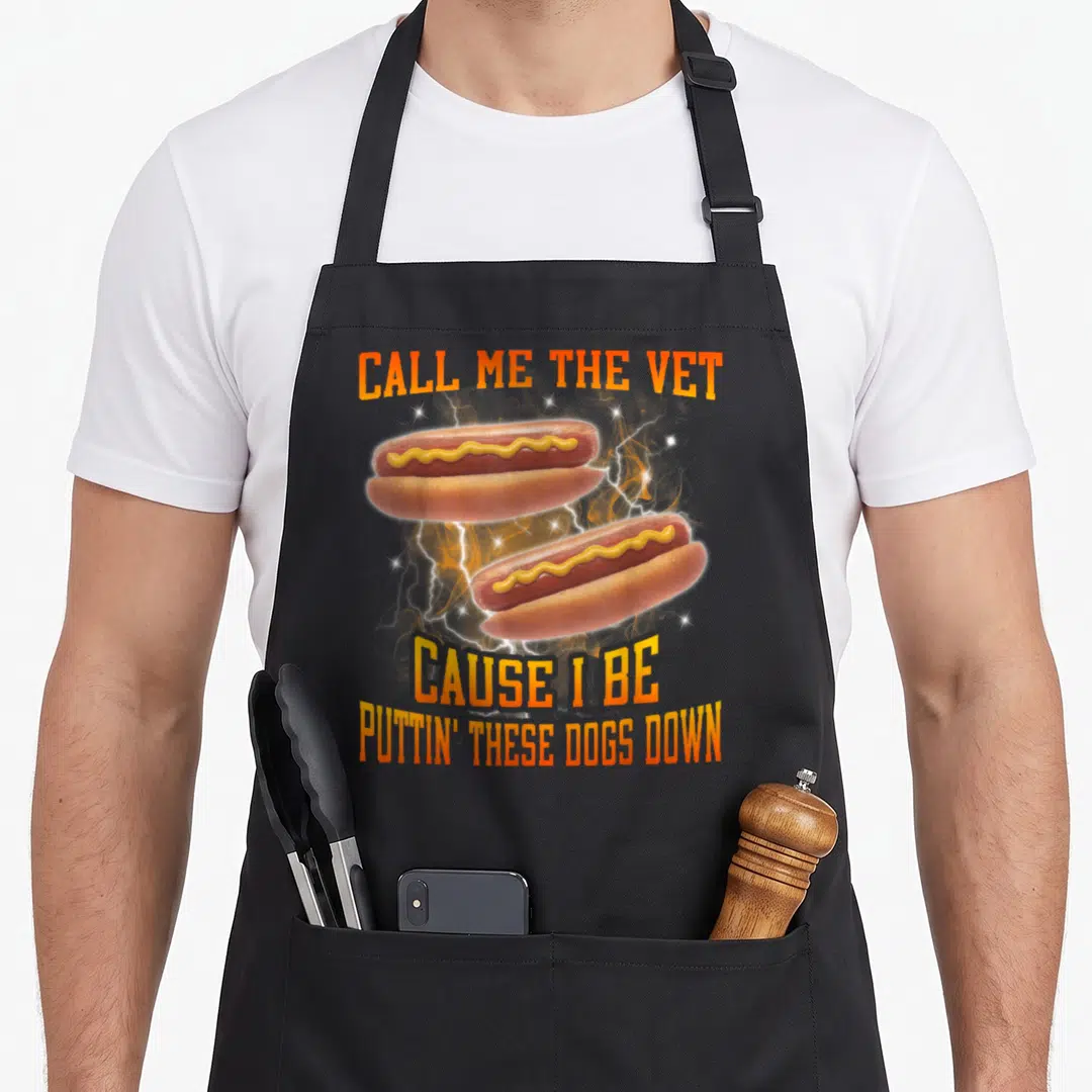Call hot dog apron - Two hot dogs with lightning bolts and CALL ME THE VET text in orange and yellow — shown on a black cotton canvas apron against a white background