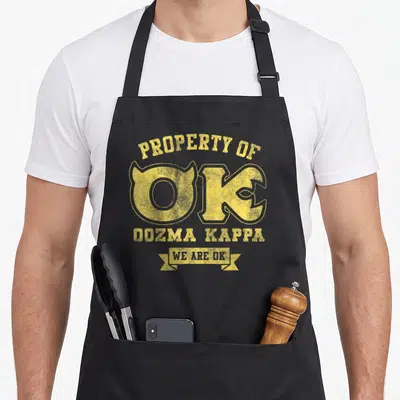 Monster monmouth university apron - Yellow distressed text reading Property of OK Oozma Kappa We Are OK stacked — shown on a black cotton canvas apron against a white background