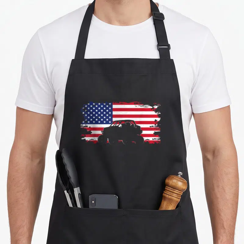 Road american flag apron - Grey off-road vehicle silhouette over distressed red white and blue USA flag — shown on a black cotton canvas apron against a white background