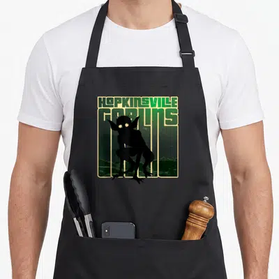 Goblin hopkinsville apron - HOPKINSVILLE GOBLINS text above a black goblin silhouette on a green landscape with beige — shown on a black cotton canvas apron against a white background