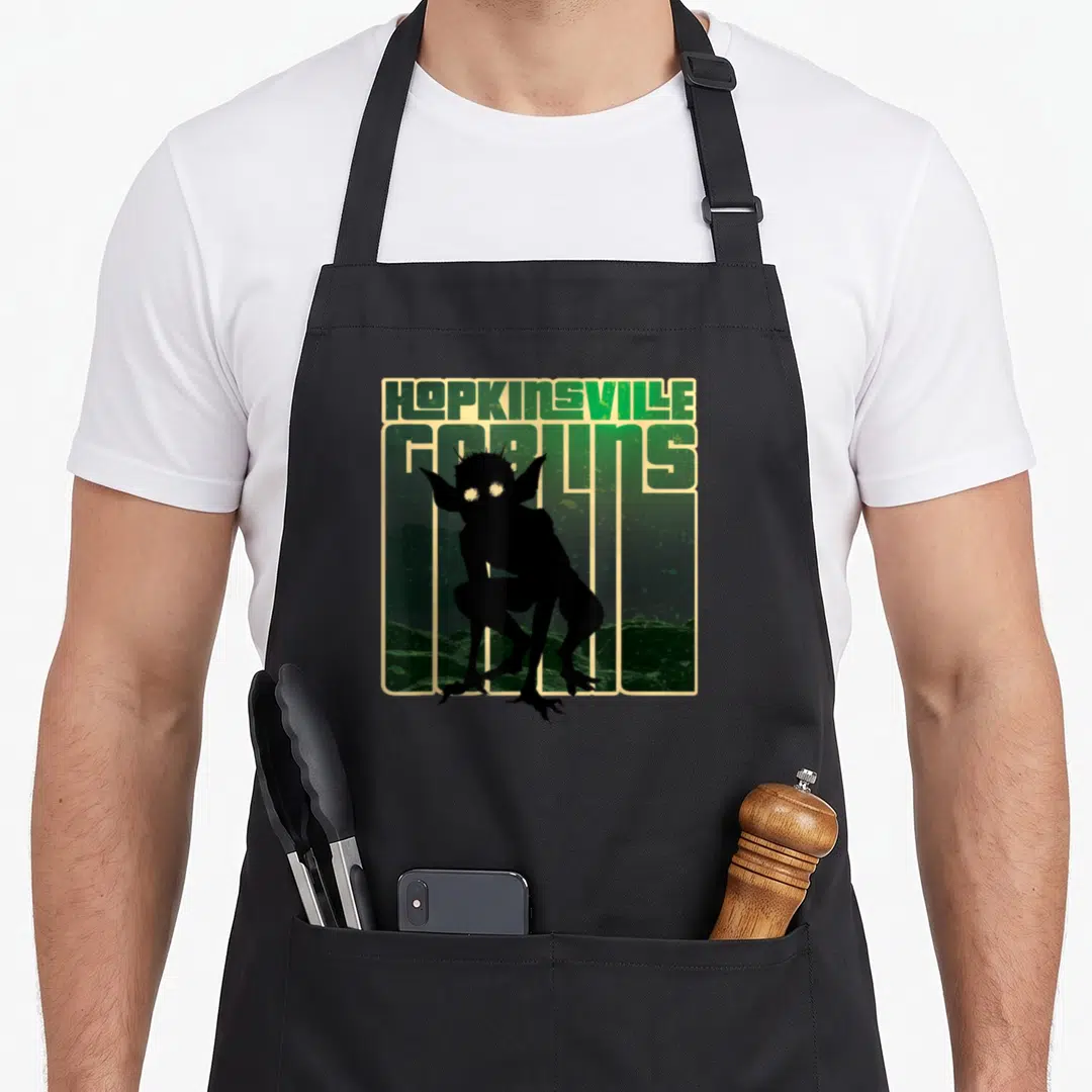 Goblin hopkinsville apron - HOPKINSVILLE GOBLINS text above a black goblin silhouette on a green landscape with beige — shown on a black cotton canvas apron against a white background