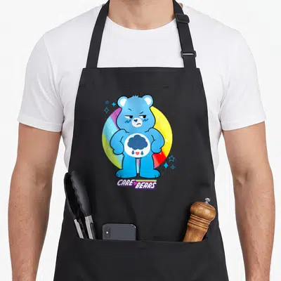 Unlock bear apron - Blue cartoon bear with raincloud belly emblem and CARE BEARS text below rainbow circle — shown on a black cotton canvas apron against a white background