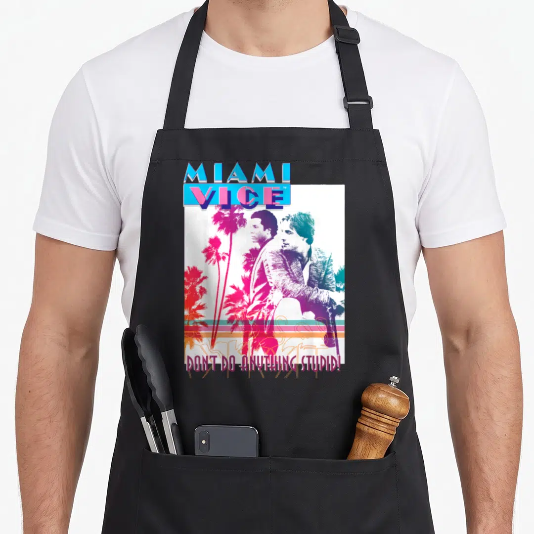 Miami stupid aprons - Retro graphic of two men and palm trees with text Don't Do Anything Stupid in pink and blue — shown on a black cotton canvas apron against a white background