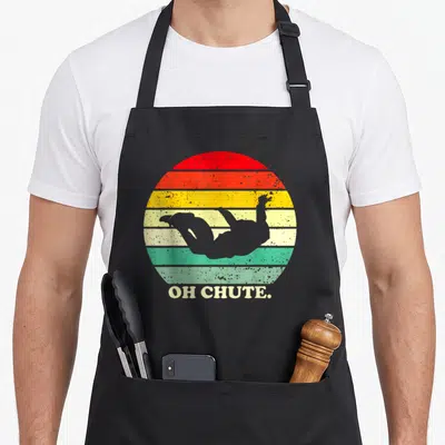 Chute sky apron - Grey skydiver silhouette over red orange yellow green grey stripes with OH CHUTE text — shown on a black cotton canvas apron against a white background
