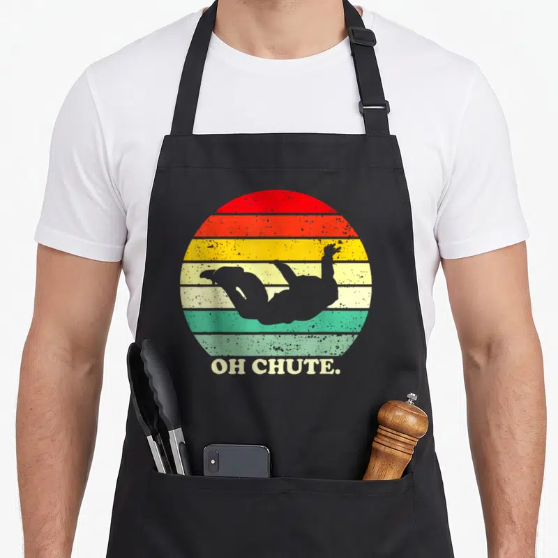 Chute sky apron - Grey skydiver silhouette over red orange yellow green grey stripes with OH CHUTE text — shown on a black cotton canvas apron against a white background