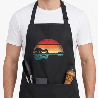 Acoustic guitar retro lovers apron - Retro sunset with red orange yellow stripes and teal landscape silhouette — shown on a black cotton canvas apron against a white background