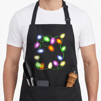 Glowing christmas tree apron - Realistic green wire with glowing green blue yellow pink and orange bulbs in a loose — shown on a black cotton canvas apron against a white background