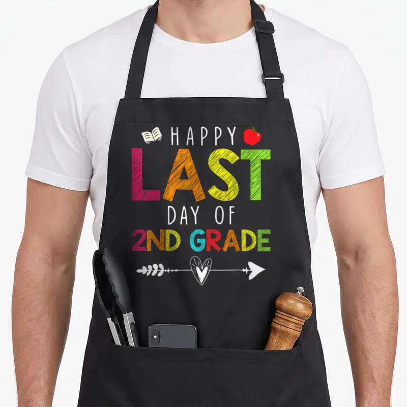 Grade teacher 2nd apron - Stacked text HAPPY LAST DAY OF 2ND GRADE with book, red apple, and heart arrow in rainbow — shown on a black cotton canvas apron against a white background