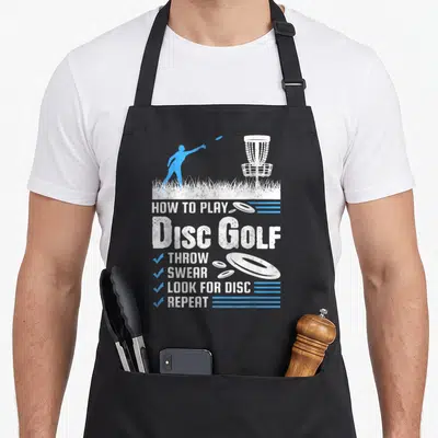 Play golf apron - Stacked white and blue text reading HOW TO PLAY DISC GOLF THROW SWEAR LOOK FOR DISC REPEAT — shown on a black cotton canvas apron against a white background