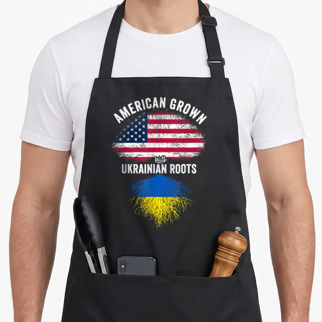 Grown ukrainian american flag apron - Plant shaped like US and Ukraine flags with AMERICAN GROWN With UKRAINIAN ROOTS — shown on a black cotton canvas apron against a white background