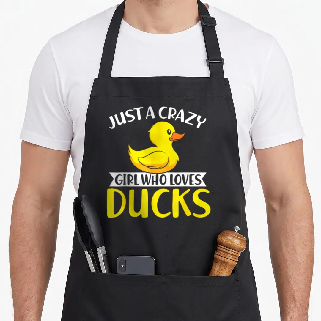 Ducky cotton duck aprons - Yellow rubber duck with white arched text and banner reading JUST A CRAZY GIRL WHO LOVES — shown on a black cotton canvas apron against a white background