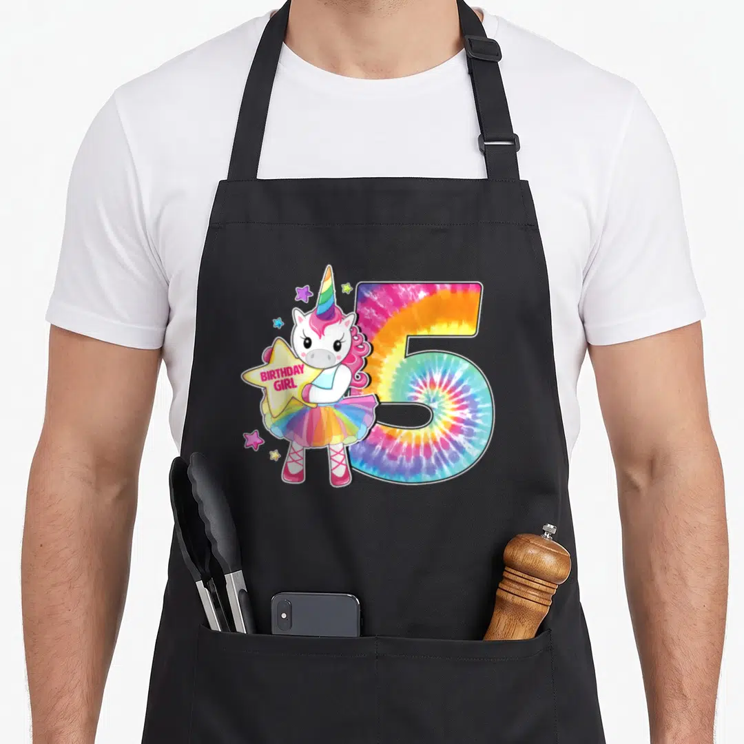 Unicorn tie-dye apron - Cartoon unicorn in tutu holding BIRTHDAY GIRL star beside tie-dye number 5 — shown on a black cotton canvas apron against a white background