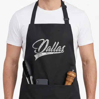 Sport texas apron - Distressed white Dallas script with underline swoosh on gray background — shown on a black cotton canvas apron against a white background