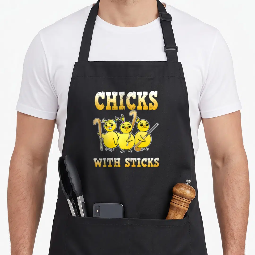 Chick field apron - Three angry yellow cartoon chicks holding field hockey sticks under arched text — shown on a black cotton canvas apron against a white background