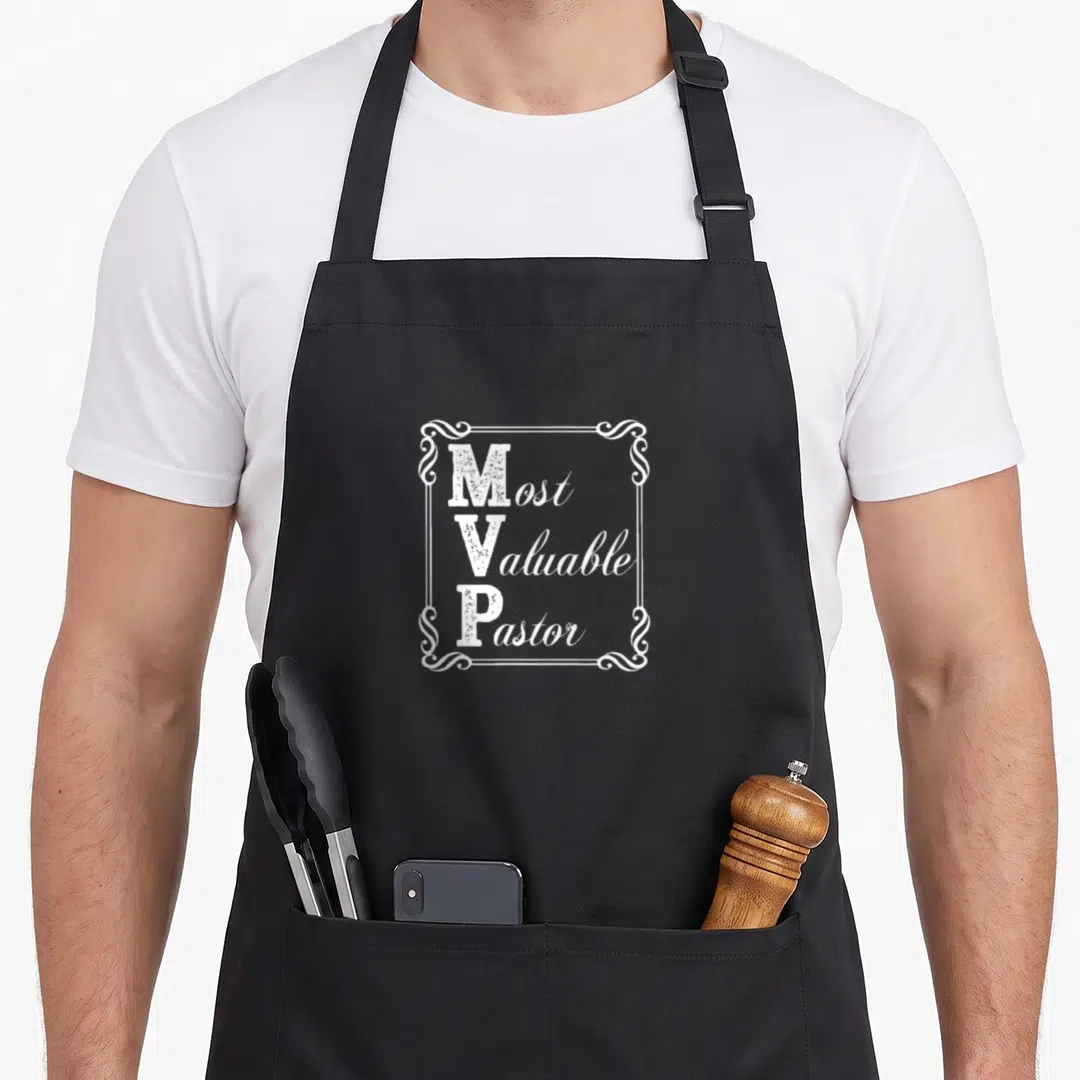 Pastor magnolia apron - White Most Valuable Pastor text in ornate border on black apron — shown on a black cotton canvas apron against a white background