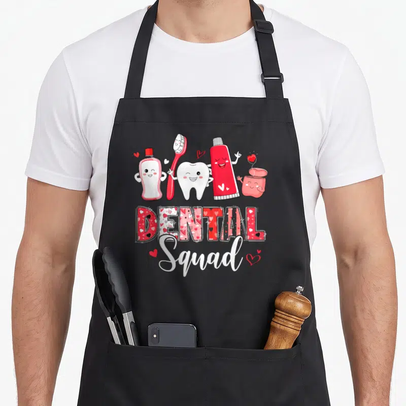 Dental valentine's day apron - Cartoon toothbrush, tooth, and toothpaste characters above patterned DENTAL Squad text — shown on a black cotton canvas apron against a white background