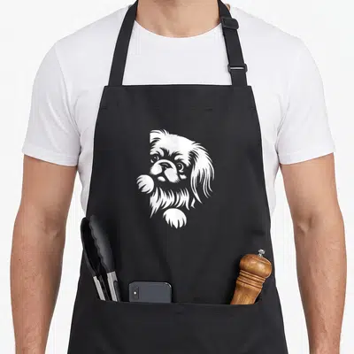 Pekingese peeking dog apron - White line art of a Pekingese dog head and paws peeking over an edge — shown on a black cotton canvas apron against a white background