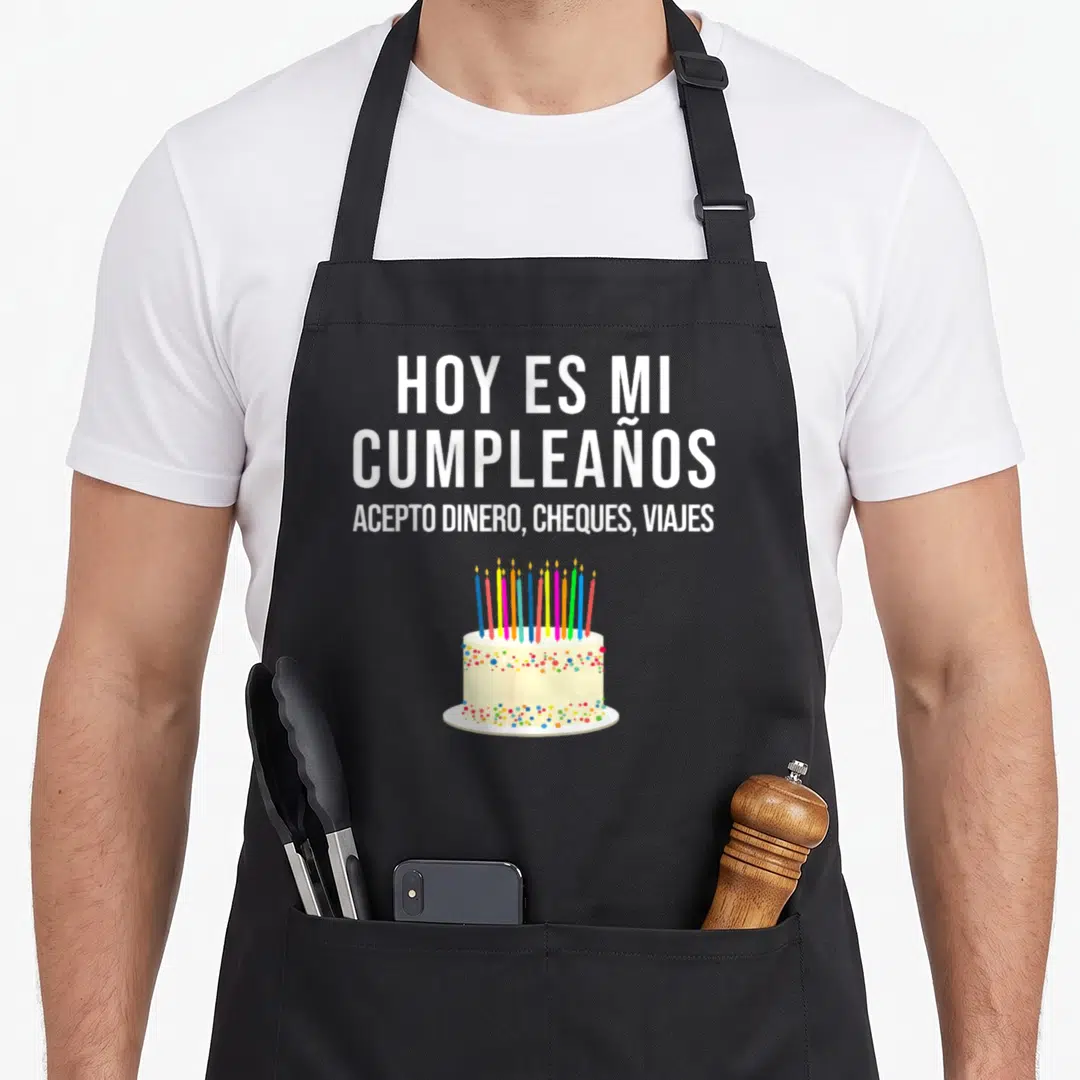 Hoy spanish aprons - White Spanish text above birthday cake with colorful sprinkles and candles — shown on a black cotton canvas apron against a white background