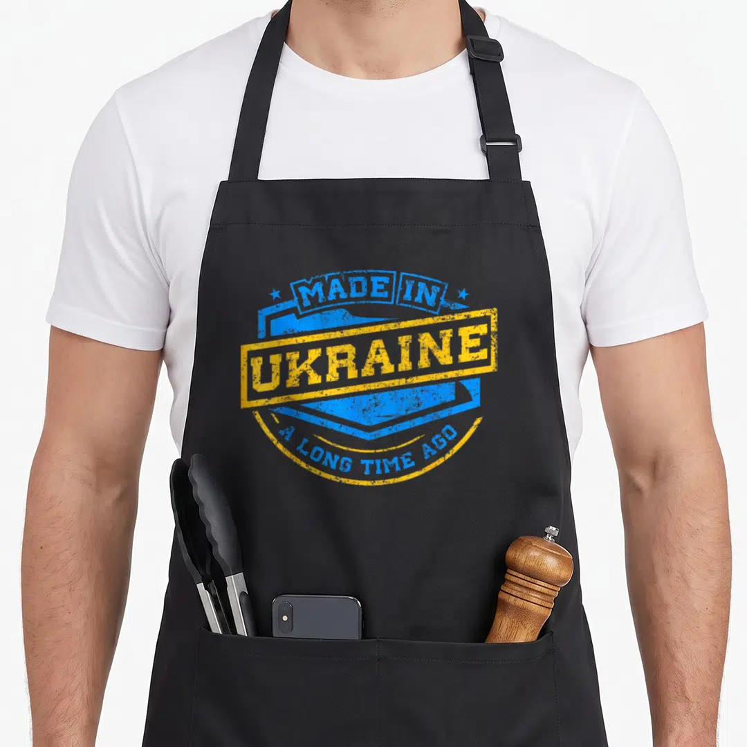 Ago ukrainian aprons - Blue and yellow distressed stamp design reading Made In Ukraine A Long Time Ago — shown on a black cotton canvas apron against a white background
