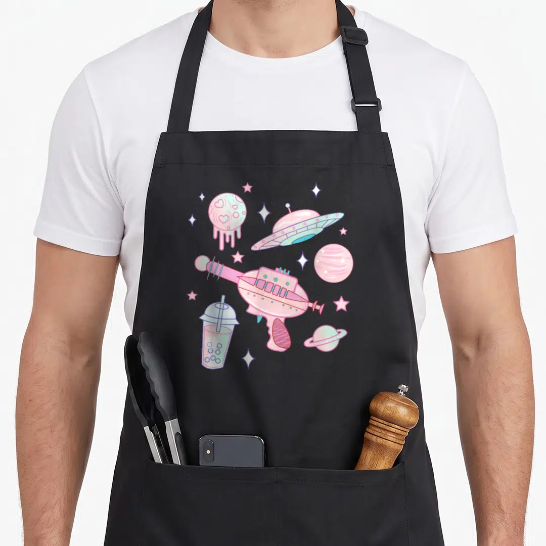 Alien goth apron - Pastel ray gun, UFO, planets, and bubble tea in a scattered cartoon arrangement — shown on a black cotton canvas apron against a white background