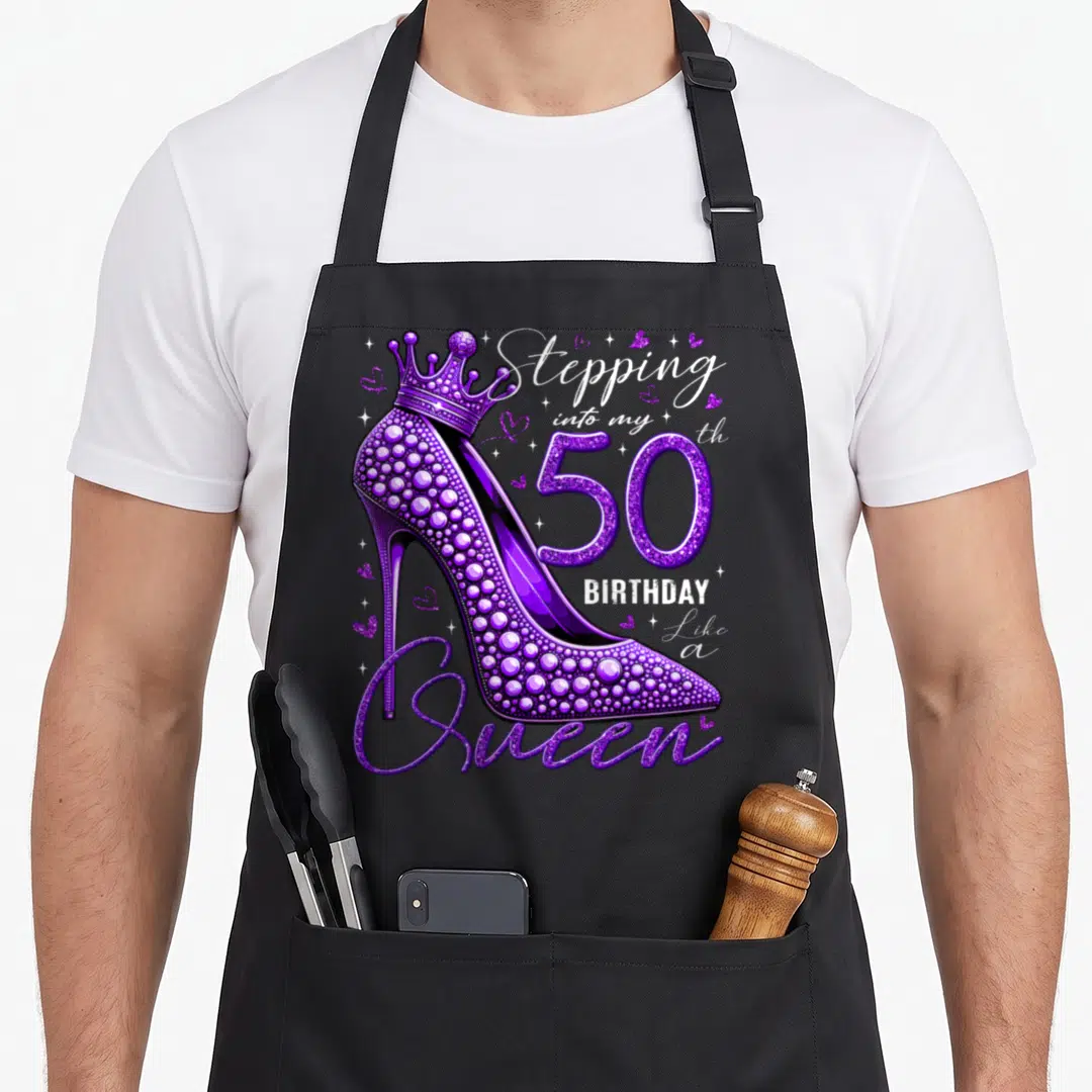 50th stepping birthday apron - Purple rhinestone high heel with crown and birthday typography text — shown on a black cotton canvas apron against a white background