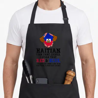 Speak creole apron - Hands tearing USA flag to show Haitian flag with stacked text HAITIAN I AM THAT CREOLE — shown on a black cotton canvas apron against a white background