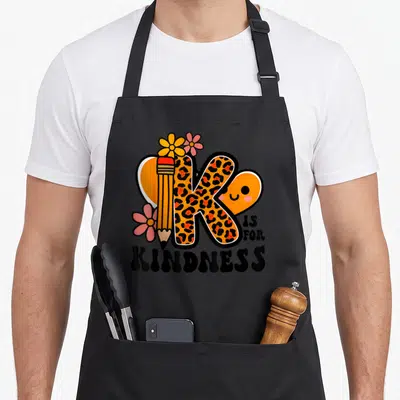 Kindness kind teacher apron - Leopard print K shaped like a pencil with flowers and IS FOR KINDNESS text — shown on a black cotton canvas apron against a white background