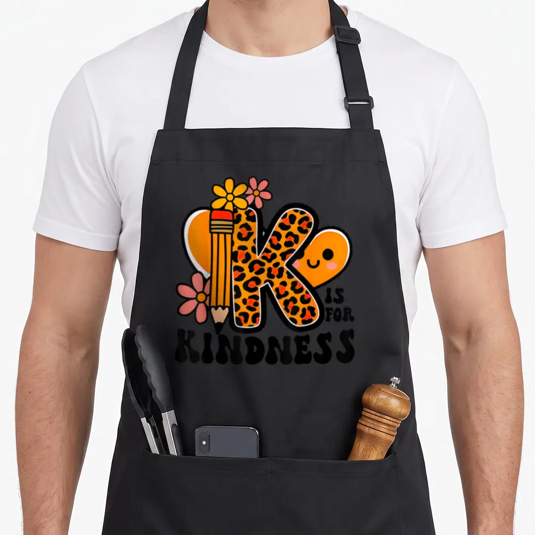 Kindness kind teacher apron - Leopard print K shaped like a pencil with flowers and IS FOR KINDNESS text — shown on a black cotton canvas apron against a white background