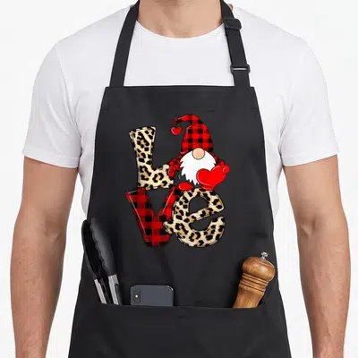 Gnome leopard apron - Cartoon gnome holding red heart on LOVE letters with leopard and plaid fills — shown on a black cotton canvas apron against a white background