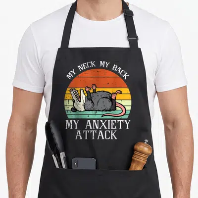 Opossum song days apron - Retro striped sun with screaming opossum lying on back and white text reading MY NECK MY BACK — shown on a black cotton canvas apron against a white background