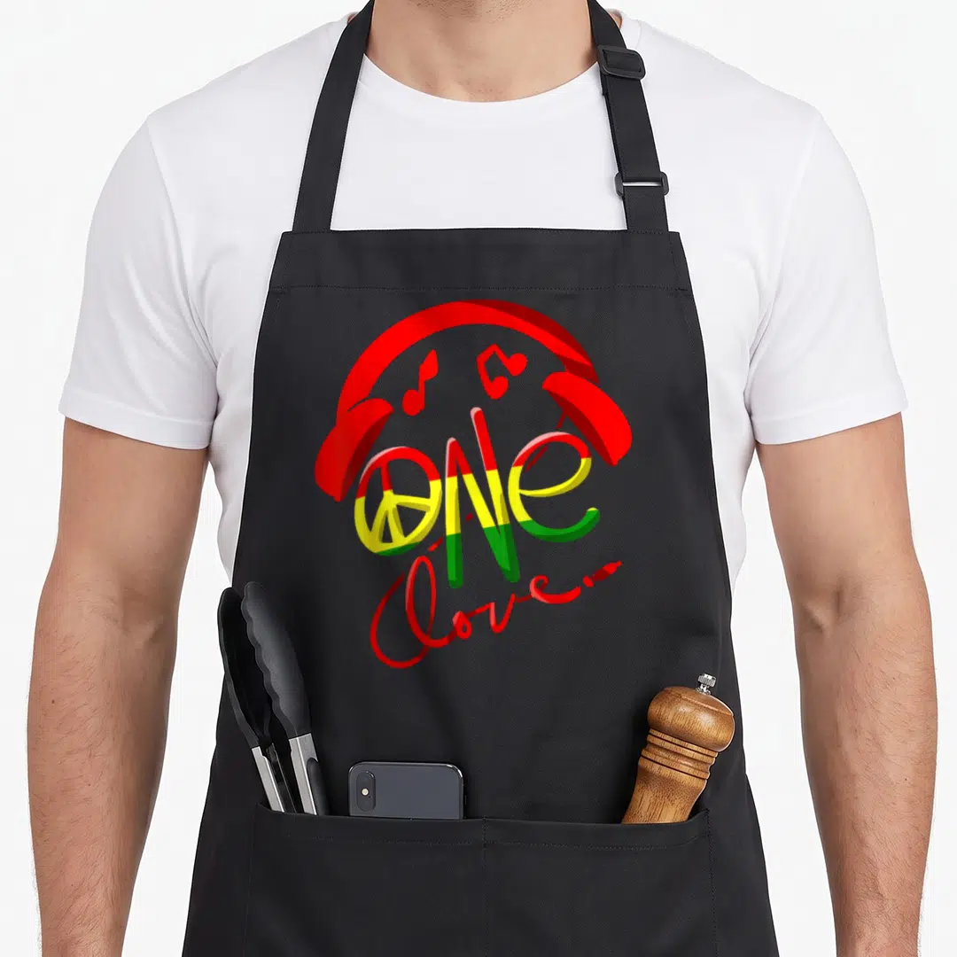 Jamaica pride apron - Red headphones arch over striped ONE and script Love... with three musical notes — shown on a black cotton canvas apron against a white background